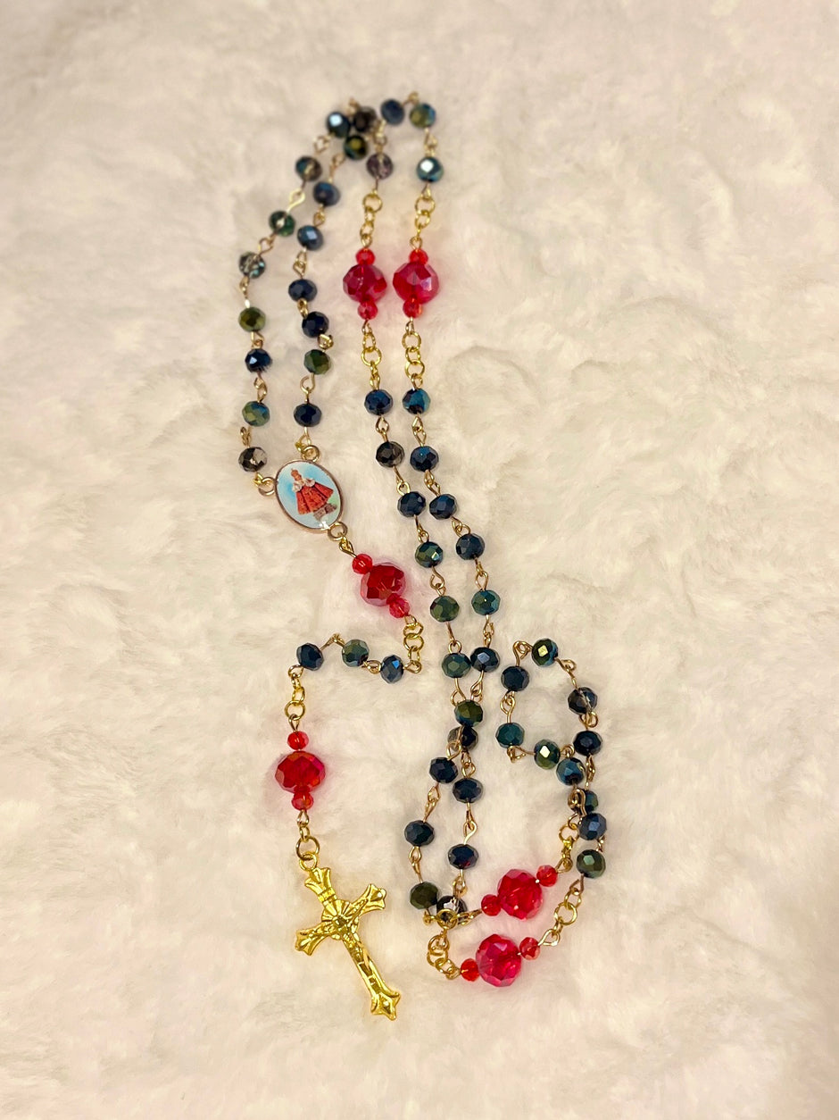 Handcrafted 5-decade dark glass rosary with red crystal Our Father beads, a Baby Jesus center medal, and a gold-toned sunburst crucifix.